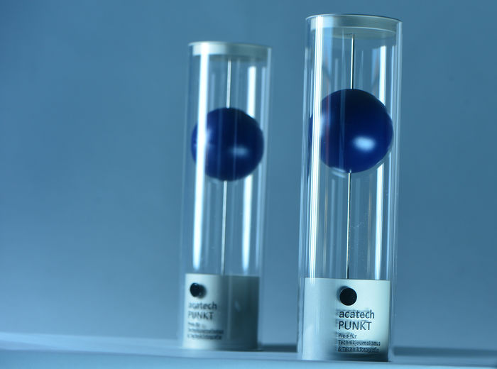 Die Trophäen für den Acatec PUNKT - Preis für Technikjournalismus & Technikfotografie. Die Trophäe ist zylinderförmig und enthält einen großen, blauen Punkt.