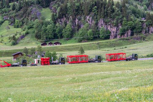 Vier LKW beladen mit Einzelteilen des WOLFFKRANs fahren durch die grüne Berglandschaft der Schweiz.