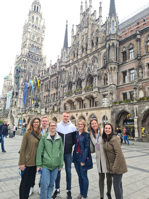 Sieben HeadlineAffairs Mitarbeiter:innen stehen vor dem Münchner Rathaus am Marienplatz und lächeln in die Kamera.