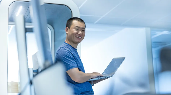 Data Engineer Ziyu Wang steht mit seinem Laptop in einem modernen Raum und lacht in richtung Kamera.