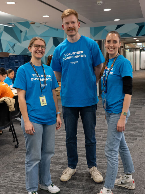 Auf dem Bild sind von links nach recht die HeadlineAffairs Mitarbeitenden Anna Wickern, Bennett Stueven und Theresa Niederstra&szlig;er zu sehen. Sie befinden sich in einem B&uuml;ro und tragen blaue T-Shirts. Sie lachen allesamt in die Kamera.